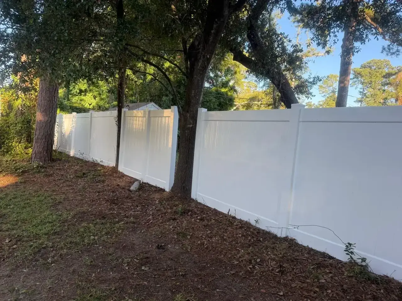 White vinyl privacy fence alongside trees